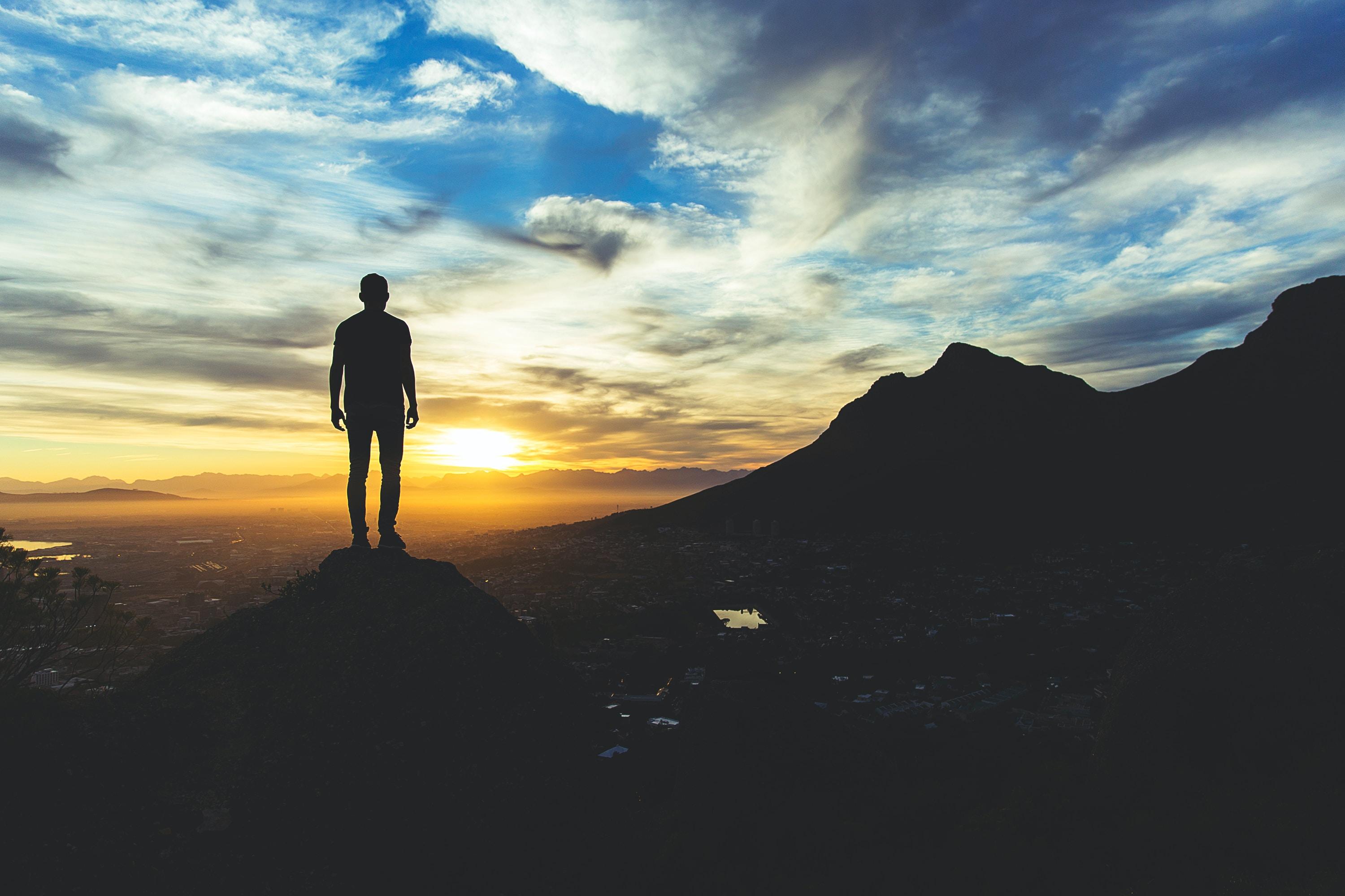 A man looking towards a mountain. We can see a city in between bathed in sunset light.